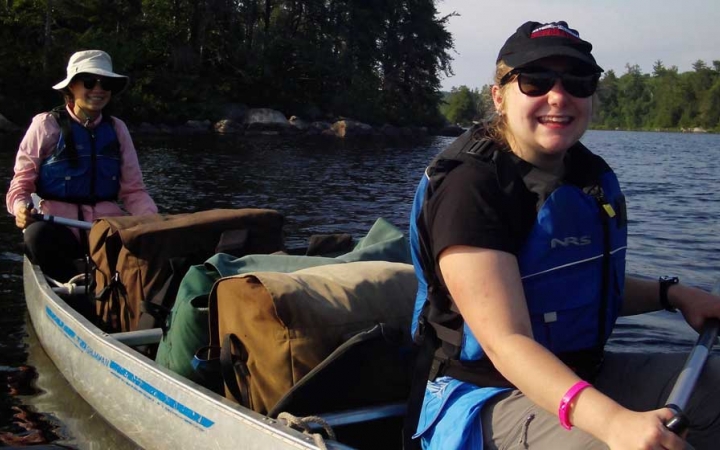 Two people wearing life jackets sit in a canoe and smile.